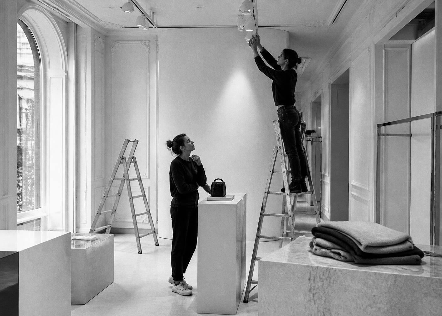 Merchandisers adjusting track lighting above a display plinth in an empty boutique